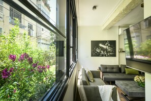Een moderne woonkamer met een bank, een salontafel en een televisie. Er is een raam met uitzicht op groen.