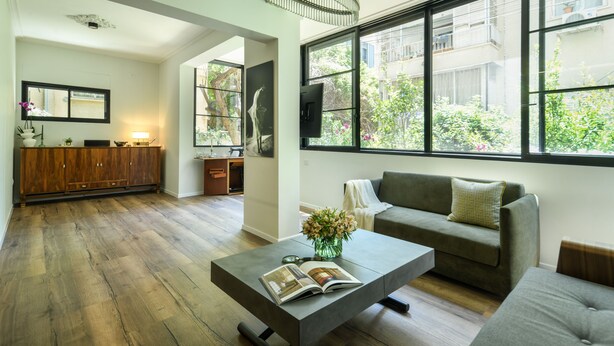 A modern living room with a sofa, coffee table, and a large window with a view of greenery. - Sophisticated Tel Aviv Retreat 1BR Apt (Tel Aviv)