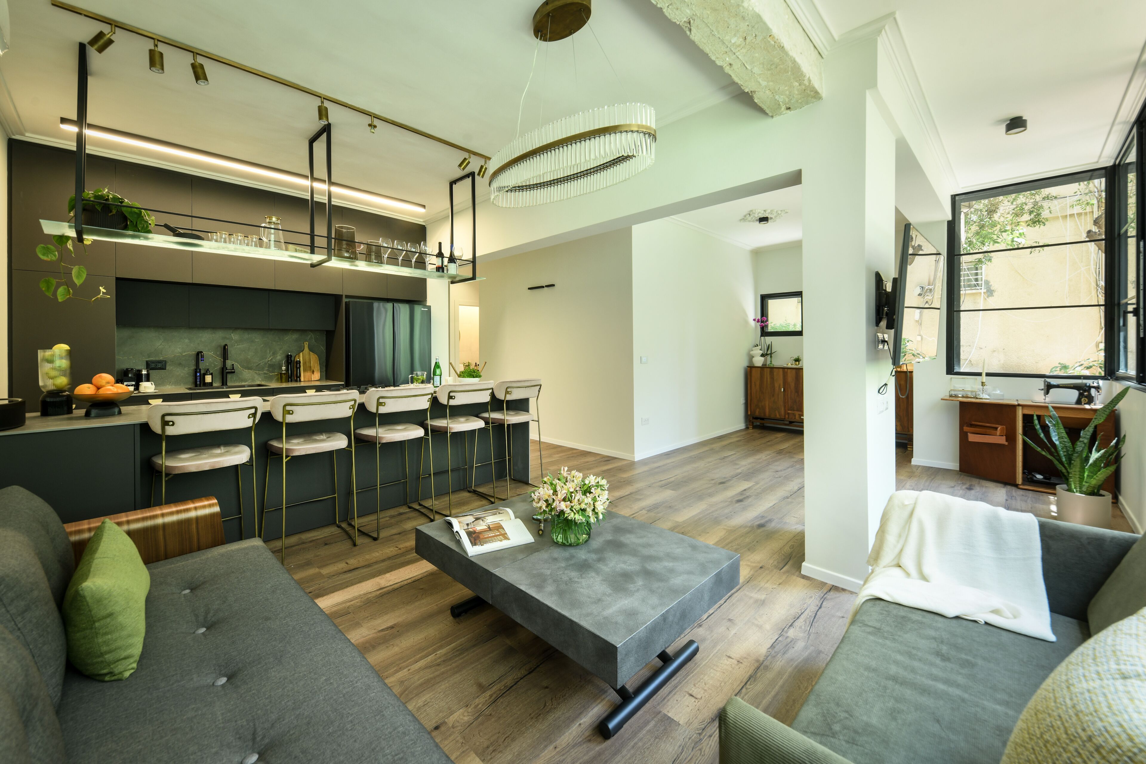 A modern kitchen with bar stools, a dining area with a grey sofa, and a large window.