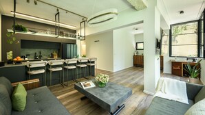 A modern kitchen with bar stools, a dining area with a grey sofa, and a large window. - Sophisticated Tel Aviv Retreat 1BR Apt (Tel Aviv)