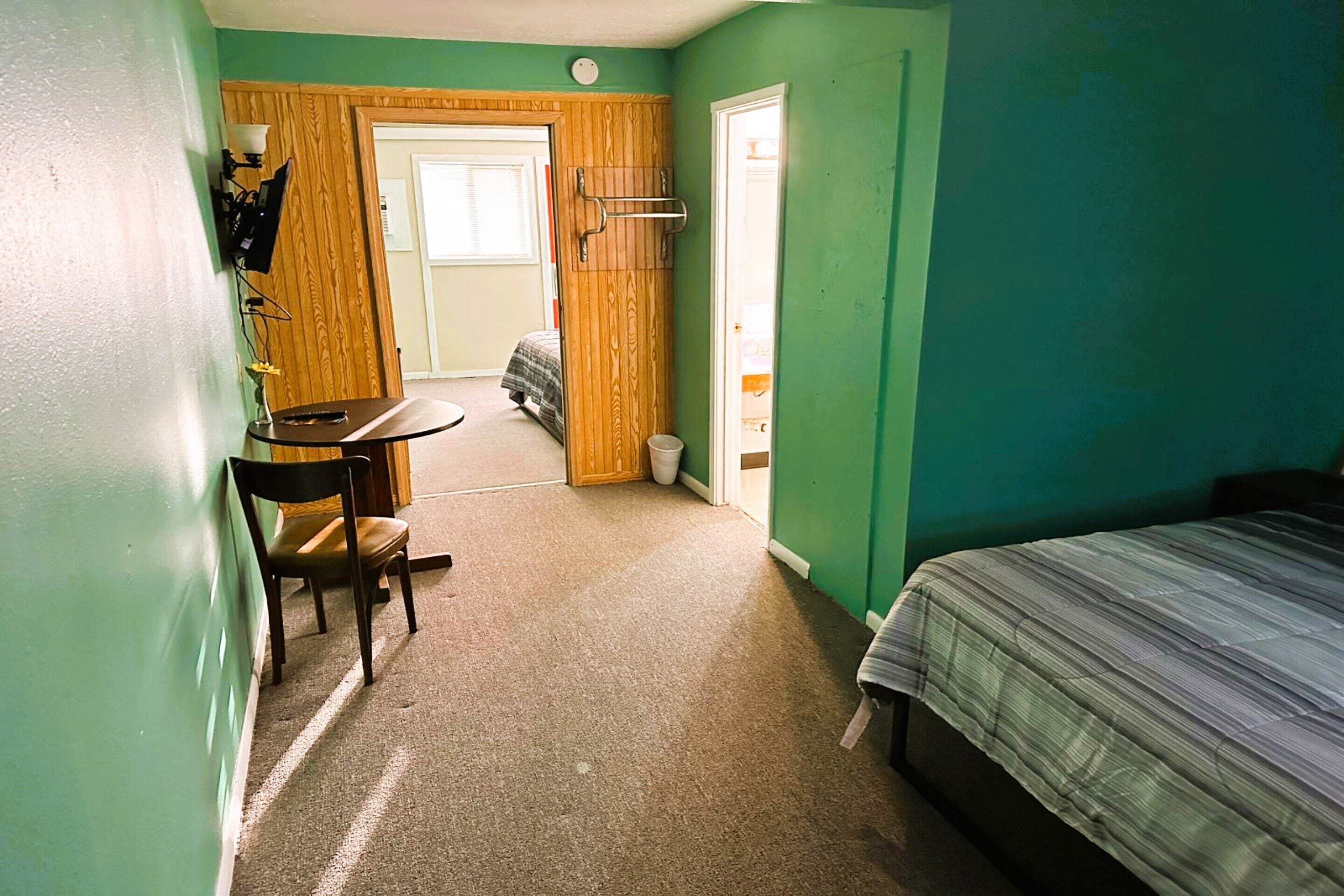 A room with a bed, a desk, and a chair. There is a door leading to another room.