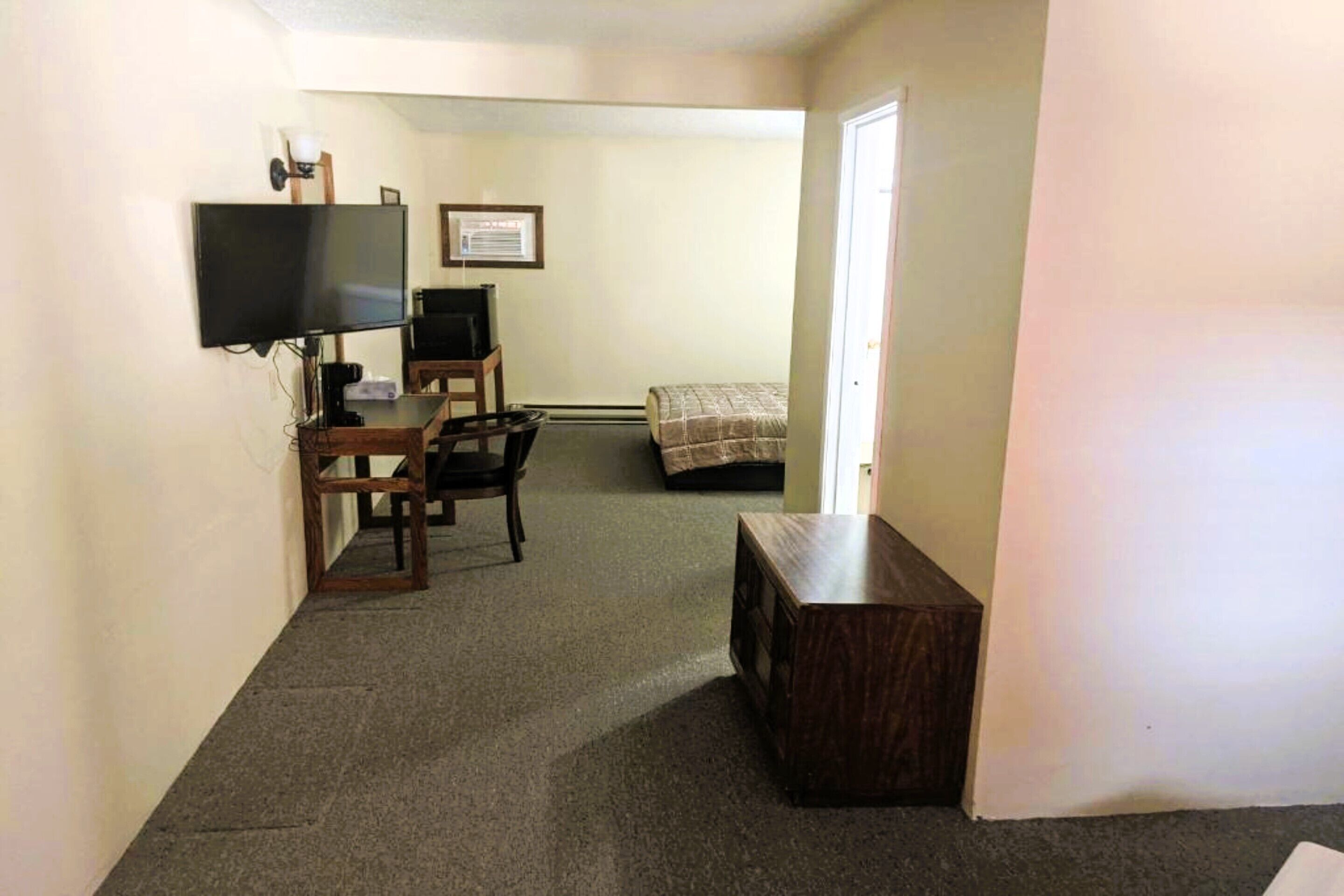 Une chambre d’hôtel comprenant un lit, un bureau avec un ordinateur, une télévision et une petite armoire en bois.