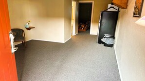 A hallway with carpeted floors, a chair, a small table with a vase, and a door leading to another room. - Badlands Motel Kadoka by OYO (Kadoka)