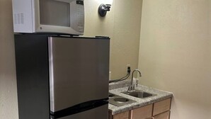 A compact kitchen with a stainless steel refrigerator, a microwave, a sink, and wooden cabinets. - Badlands Motel Kadoka by OYO (Kadoka)