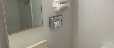 Uma casa de banho com lavatório de mármore, sanita, porta-toalhas com toalhas dobradas, espelho e dispensador de papel.