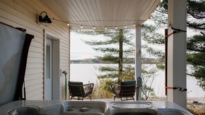 Ein Whirlpoolbereich mit zwei Korbstühlen, die auf einen See ausgerichtet sind, unter einer überdachten Terrasse mit Lichterketten.