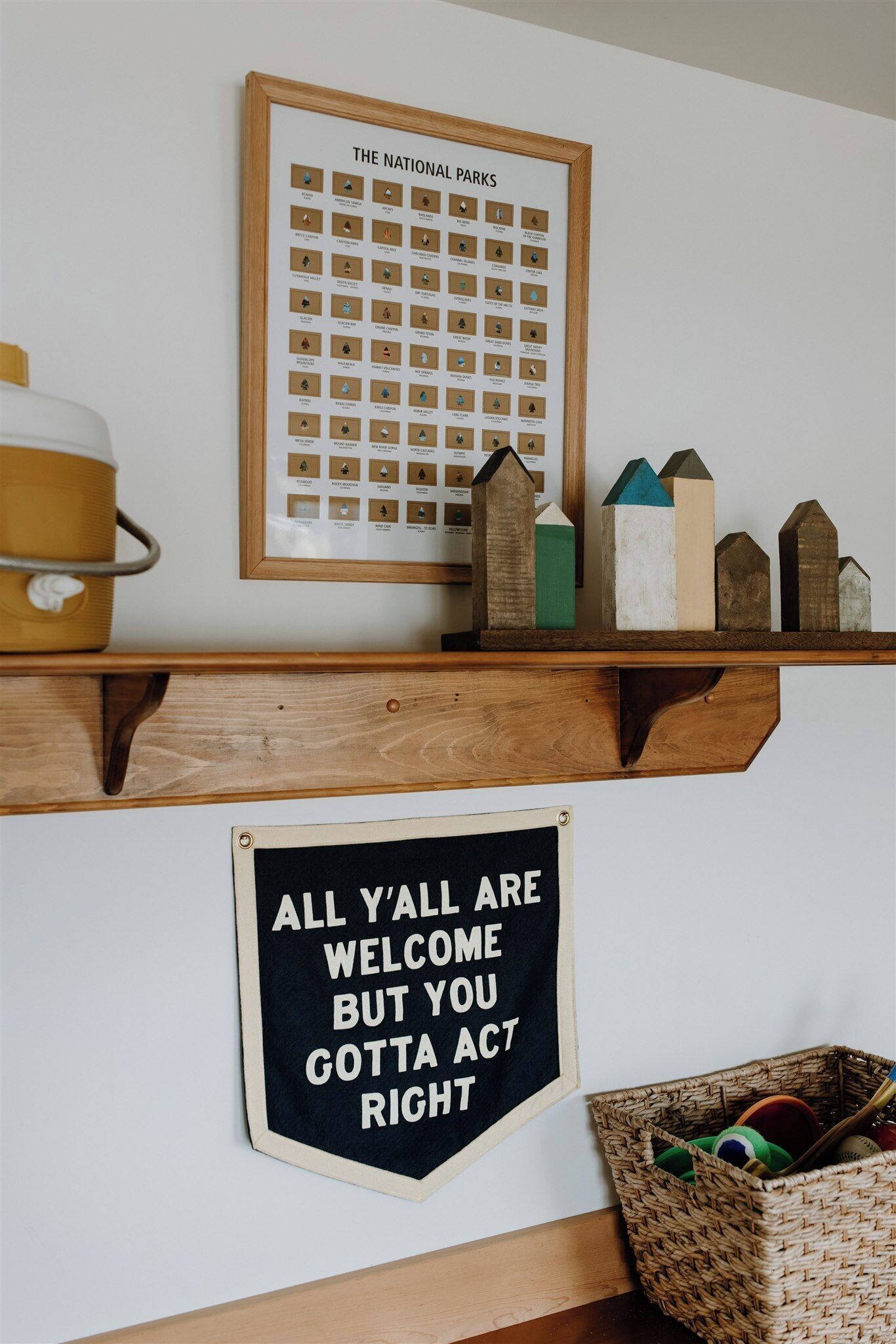 A framed poster of national parks, a wooden shelf with decorative items, and a motivational sign below.