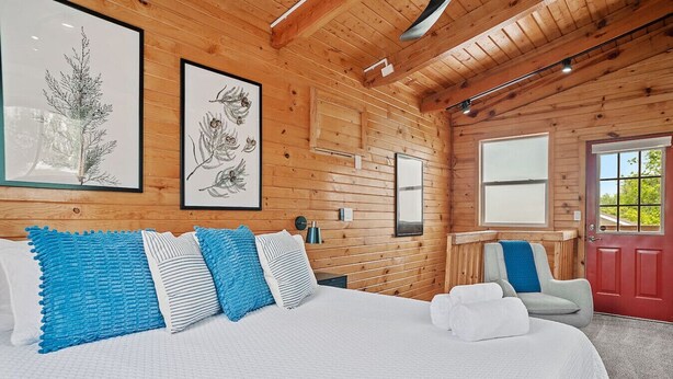 A wooden cabin bedroom with a bed, pillows, a chair, and a door.