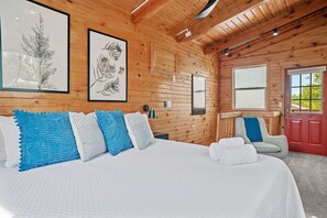 Une chambre dans une cabane en bois, avec un lit, des oreillers, une chaise et une porte.