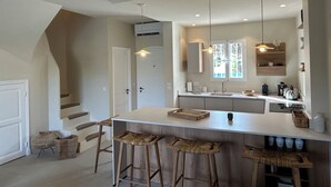A modern kitchen with a central island, bar stools, pendant lighting, and a window with a view. - Villa Rénovée Avec Piscine et Amarrage, Dans Domaine Sécurité, Avec Plage à 5 mn (Port Grimaud)