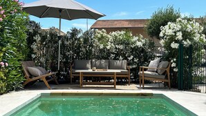 A pool area with a wooden table and two chairs, surrounded by lush greenery and white flowers. - Villa Rénovée Avec Piscine et Amarrage, Dans Domaine Sécurité, Avec Plage à 5 mn (Port Grimaud)