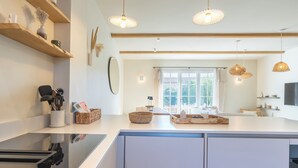 A modern kitchen with white cabinets, wooden beams, and pendant lighting. - Villa Rénovée Avec Piscine et Amarrage, Dans Domaine Sécurité, Avec Plage à 5 mn (Port Grimaud)