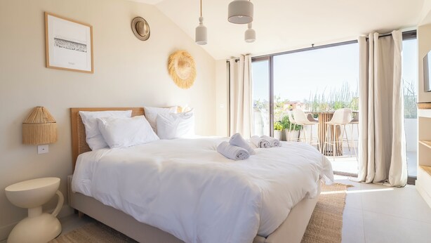 A spacious bedroom with a large bed, a bedside lamp, a framed picture on the wall, and a view of the outdoors through the window. - Villa Rénovée Avec Piscine et Amarrage, Dans Domaine Sécurité, Avec Plage à 5 mn (Port Grimaud)