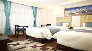A hotel room with two beds, a desk, a chair, and a large mountain view painting. - MeroStay204Satkar hotel (Kathmandu)