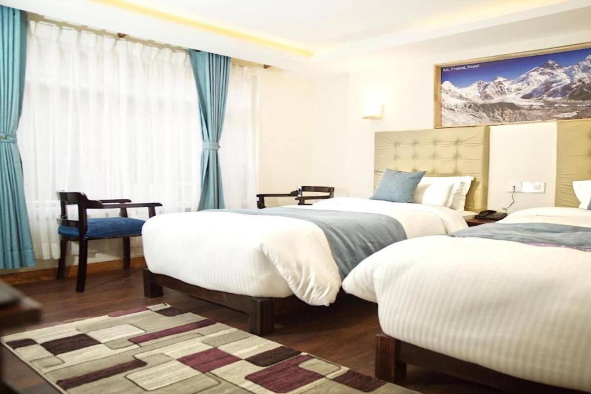 Habitación de hotel con dos camas, un escritorio, una silla y un cuadro de un extenso paisaje montañoso.