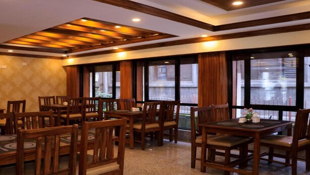 A restaurant with wooden tables and chairs, large windows with curtains, and a patterned wall. - MeroStay204Satkar hotel (Kathmandu)