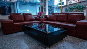 A modern living room with a brown leather sectional sofa, a black glass coffee table, and a vase with pink flowers. - MeroStay204Satkar hotel (Kathmandu)