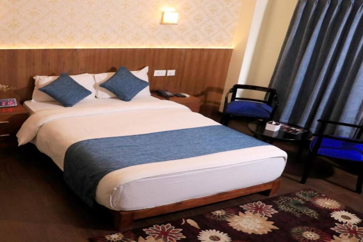 Una habitación de hotel con una cama grande, una mesita de noche con un reloj, una silla y un escritorio con una lámpara.