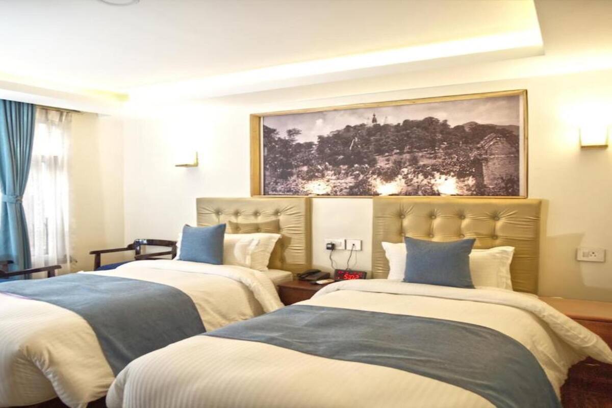Una habitación de hotel con dos camas, un cuadro grande en la pared y una ventana con cortinas.
