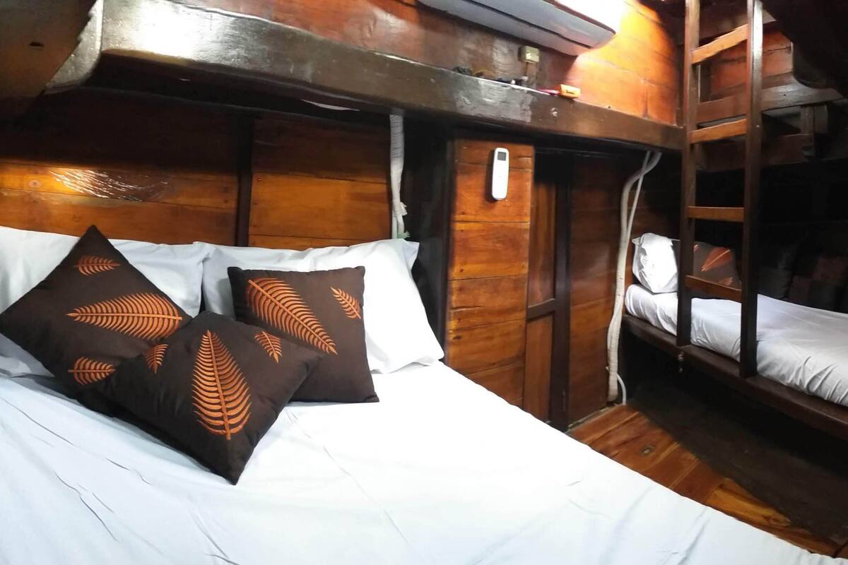 Ein Schlafraum mit Etagenbett, Holzwänden und einem Einzelbett mit weißer Bettwäsche und gemusterten Kissen.