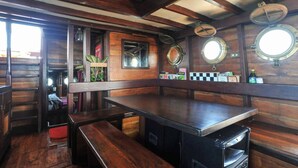 A rustic bar area with wooden walls, a long counter, and several stools. - Komodo Pirate Boat - Phinisi Liveaboard (Labuan Bajo)