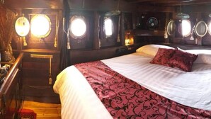 A cabin with a bed, wooden walls, and round windows. - Komodo Pirate Boat - Phinisi Liveaboard (Labuan Bajo)