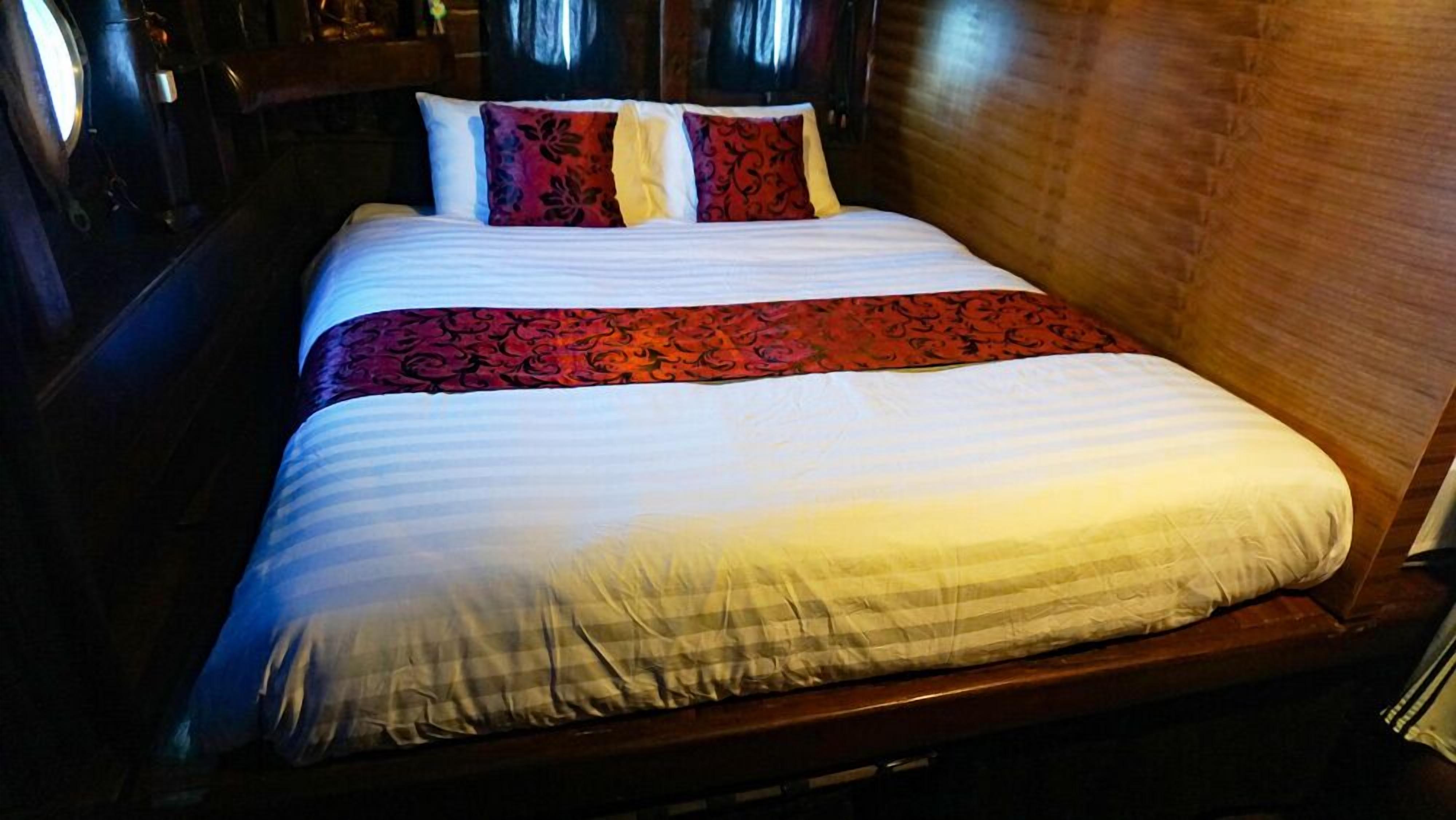 Un lit avec une couvre-lit blanche et rouge, une tête de lit en bois et un mur en bois.