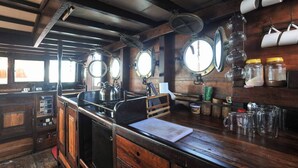 A kitchen with wooden cabinets, a stove, and a sink. There are jars and mugs on the counter. - Komodo Pirate Boat - Phinisi Liveaboard (Labuan Bajo)