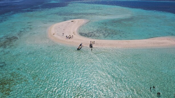 An aerial view of a beach with clear turquoise waters and a sandy shore. - Komodo Pirate Boat - Phinisi Liveaboard (Labuan Bajo)