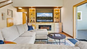 A living room with a sectional sofa, a fireplace, a flat-screen TV, and a bookshelf.