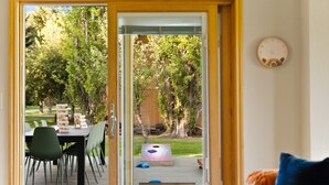 A view through a glass door into a backyard with a dining table, chairs, and a wooden deck.