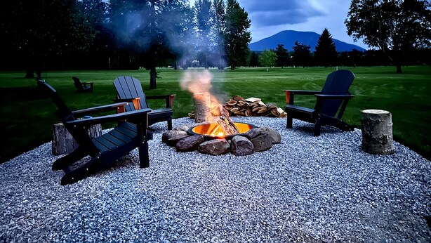 A fire pit surrounded by Adirondack chairs in a park with a mountain in the background.