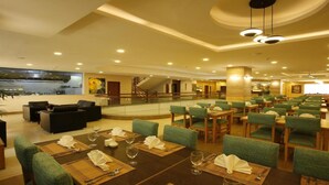 Um amplo hall de hotel com várias áreas de refeições, uma escadaria e vista para a cozinha.