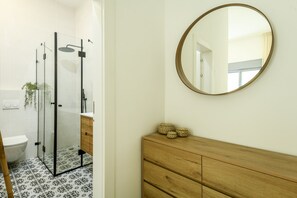 A bathroom with a glass-enclosed shower, a wooden vanity, and a round mirror on the wall. - Spacious 3BR Apt w Garden Ramat Hasharon (Ramat Hasharon)