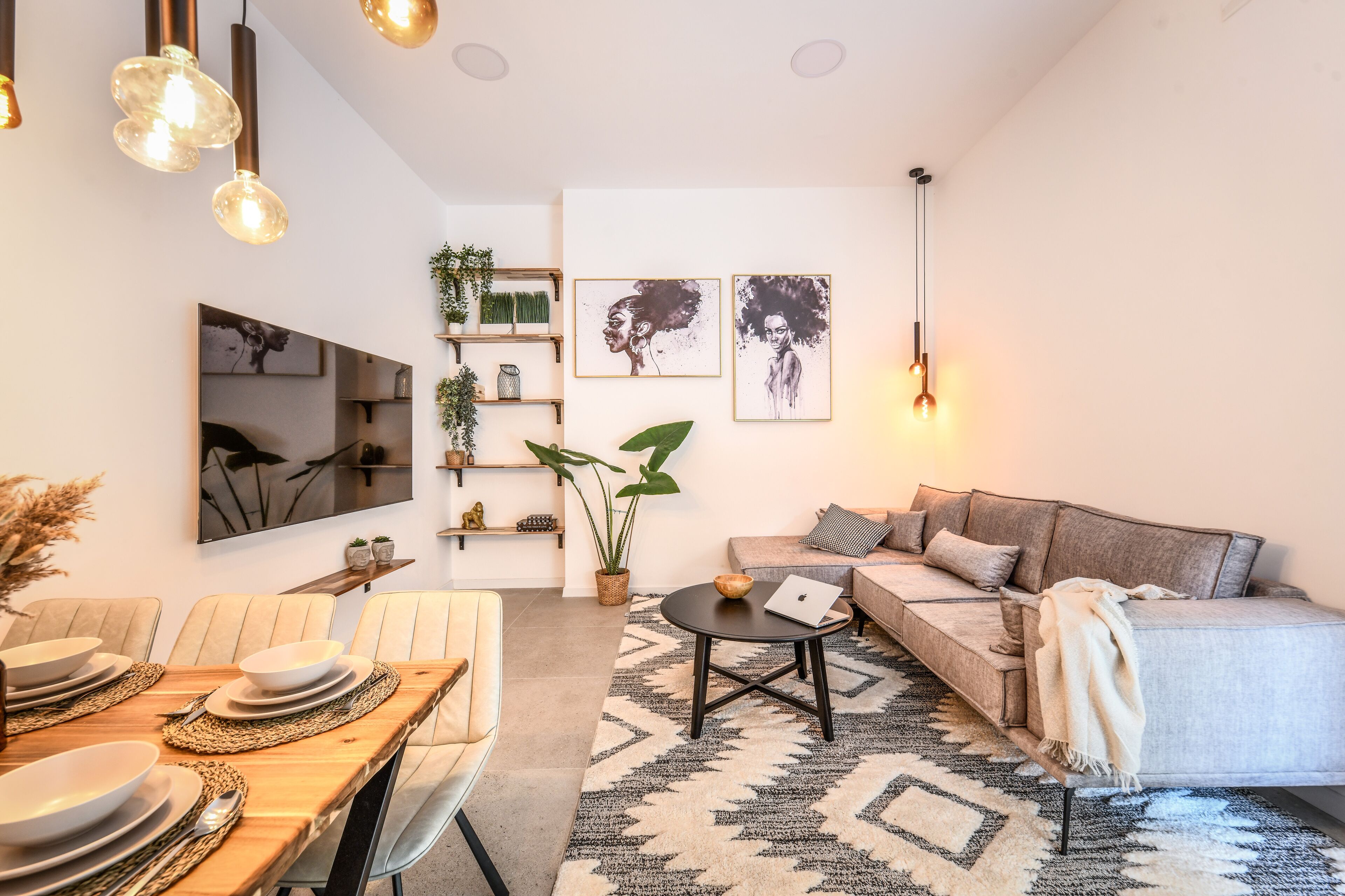 A modern living room with a sofa, dining table, and a TV mounted on the wall.