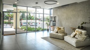 A modern lobby with a glass door entrance, a sofa with decorative pillows, and a small table with a plant. - Spacious 3BR Apt w Garden Ramat Hasharon (Ramat Hasharon)