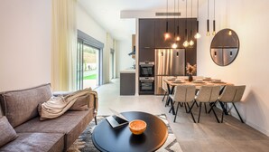 A modern living room with a sofa, a coffee table, and a dining area with chairs and a table. - Spacious 3BR Apt w Garden Ramat Hasharon (Ramat Hasharon)