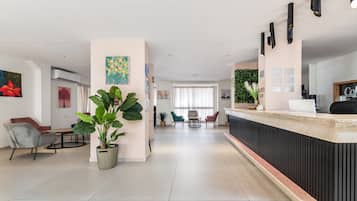 Een moderne hotellobby met een receptiebalie, zithoek en grote potplanten.