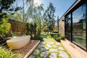 Relax in a serene outdoor space surrounded by lush greenery and a stone pathway, featuring a bathtub on a bed of pebbles.