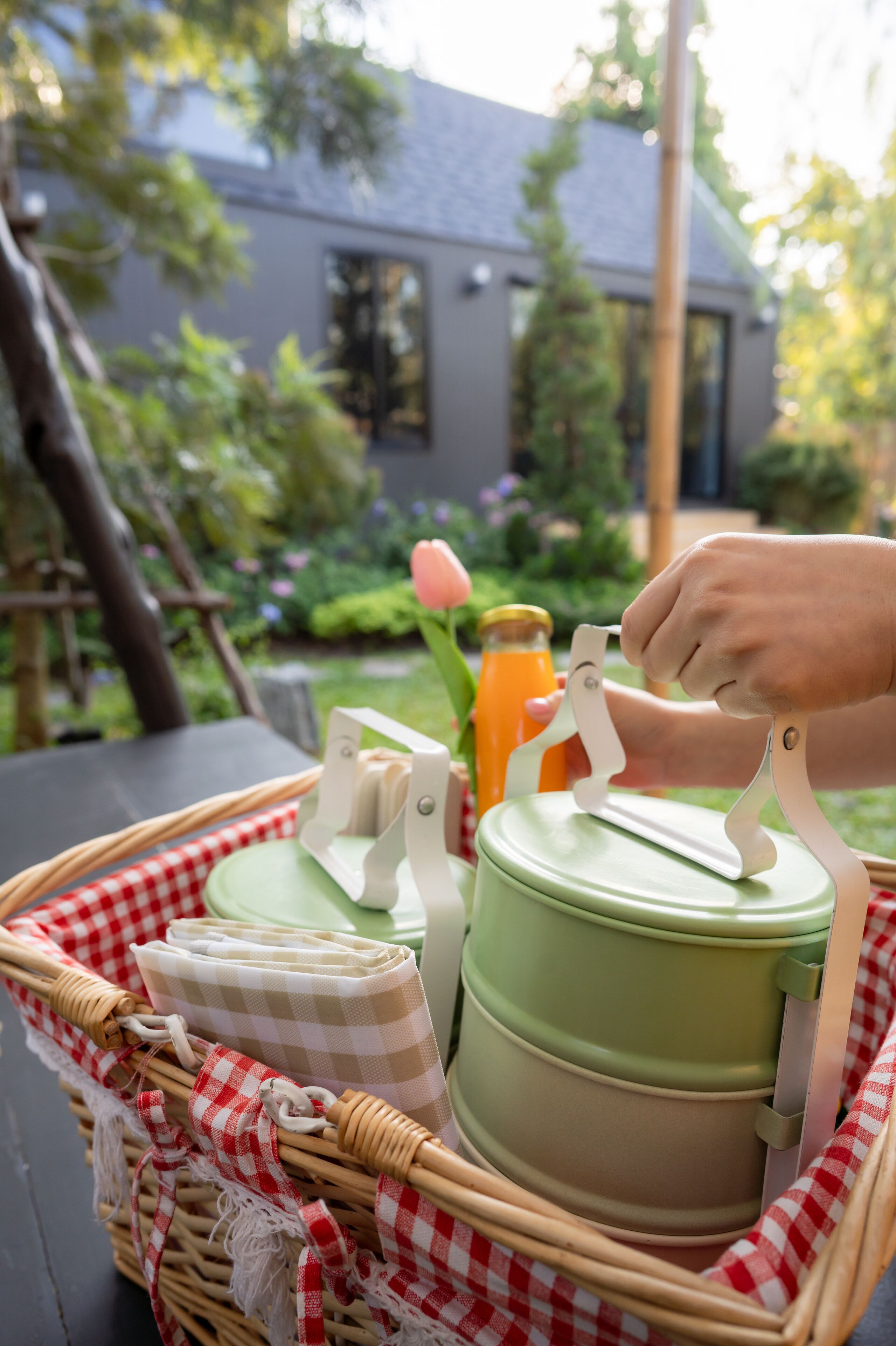 Un coin pique-nique avec un panier contenant un récipient vert, une serviette et une bouteille de jus d’orange.