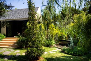 Stroll through the serene garden, featuring a weeping willow and lush greenery, to the modern building with a tiled roof.