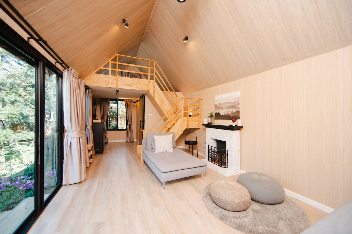 Une chambre de style loft moderne, avec un escalier en bois, un grand lit, une cheminée et une vue sur la verdure.