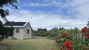 A small, single-story house with a sloped roof and a fenced yard. - Prvt cottage + cabin + pool on quarter acre section (wood burner, pet friendly) (Greytown)