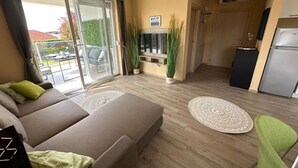 A modern living room with a sofa, a dining table, and a kitchen area with a refrigerator.
