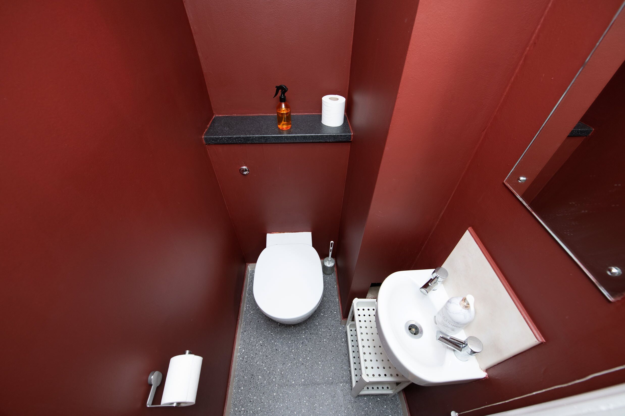 Ein kleines Badezimmer mit Toilette, Waschbecken und Ablagefläche mit Flasche und Toilettenpapier.