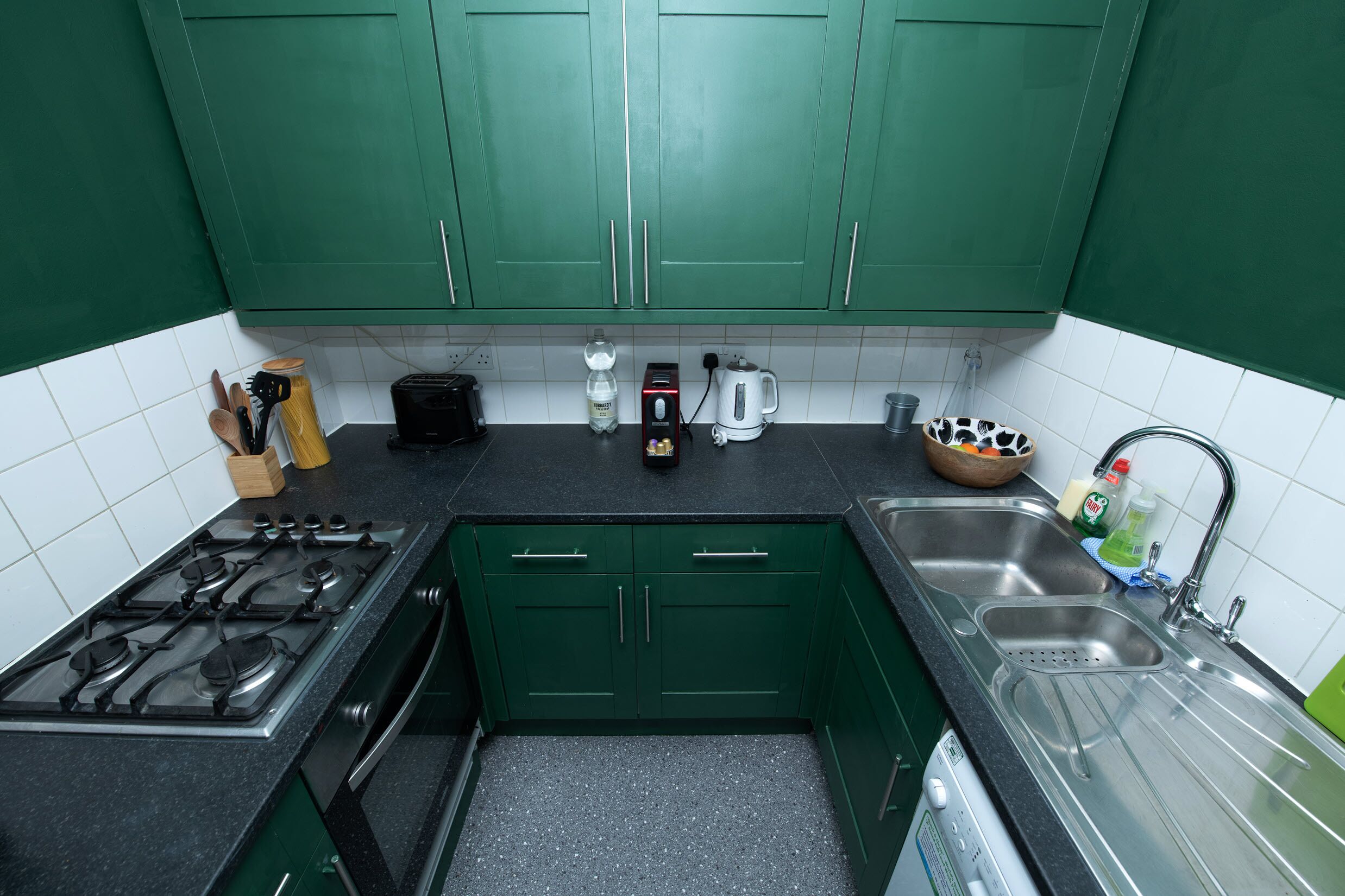 A kitchen with green cabinets, a gas stove, a coffee maker, and a sink.