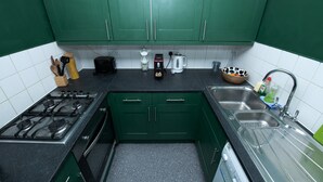 Cucina con mobili verdi, piano cottura a gas, macchina per il caffè e lavello.