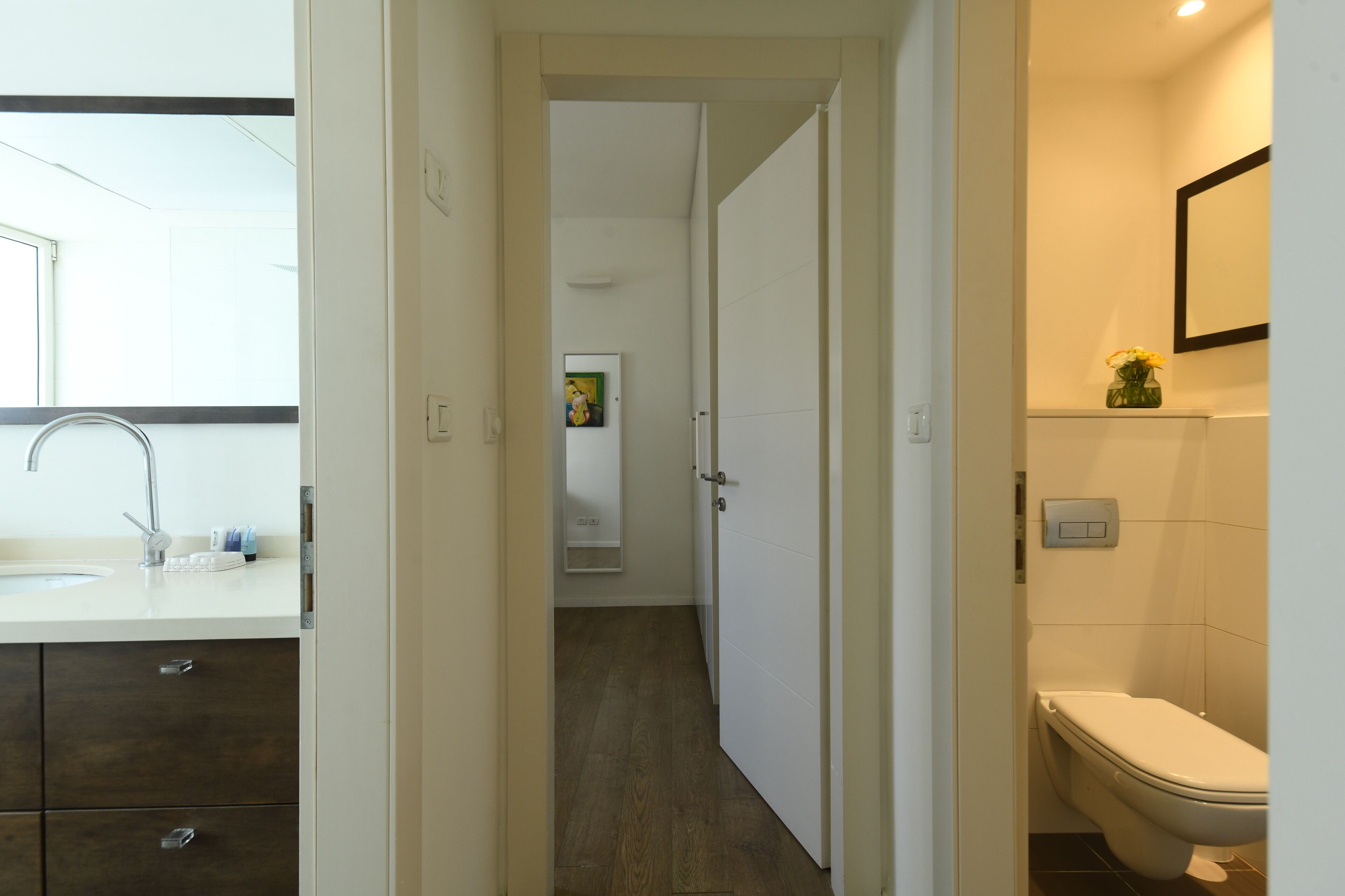 A modern bathroom with a white sink, dark wooden cabinets, a white toilet, and a mirror above the toilet.