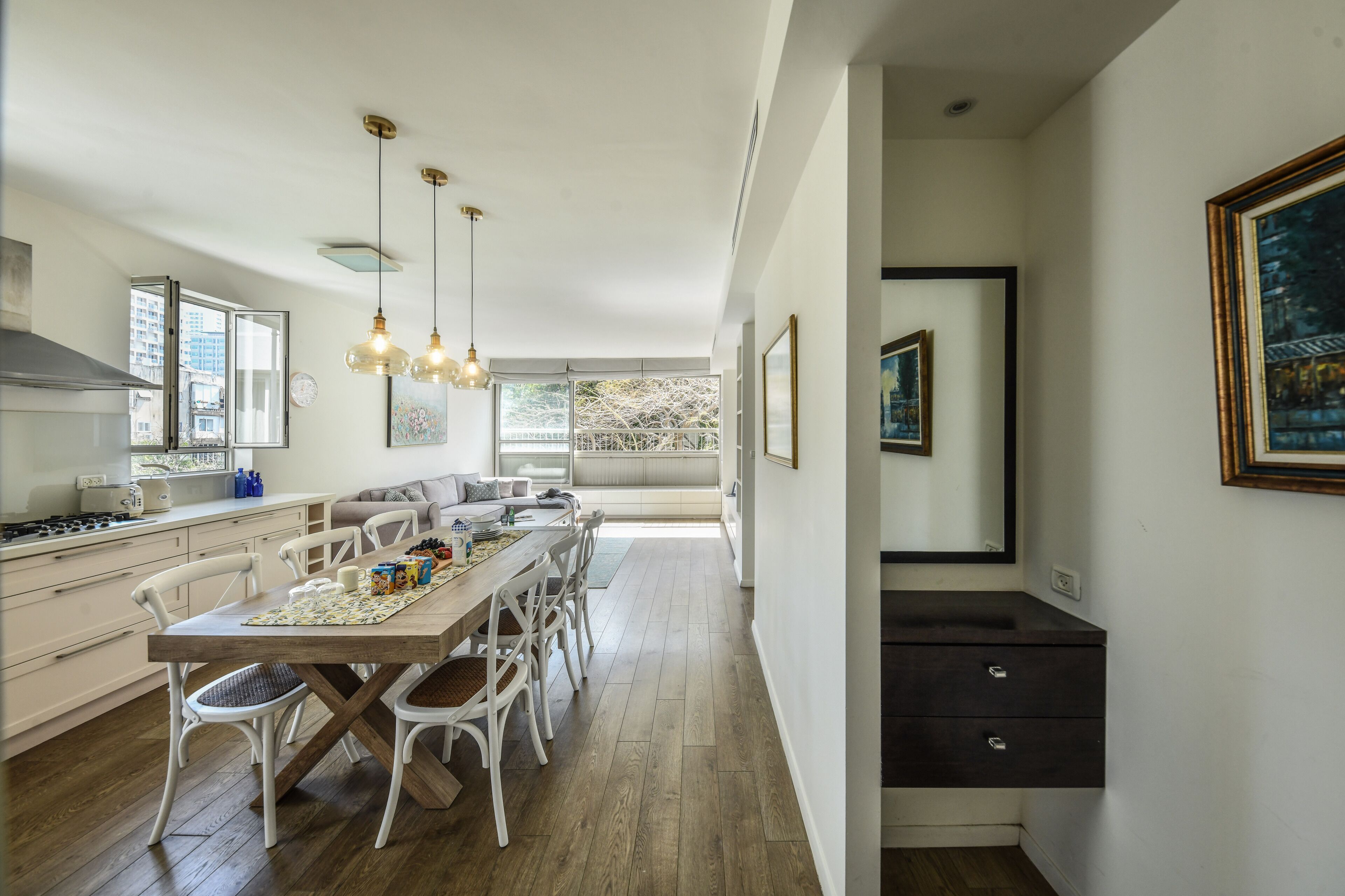 A modern kitchen with white cabinetry, a wooden dining table, and pendant lighting.