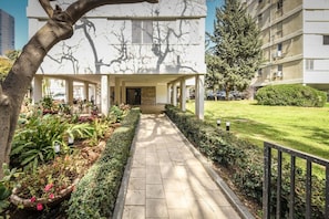 A modern building with a covered walkway, surrounded by well-maintained greenery and a clear sky. - Stunning 2BR Apartment in Beeri (Tel Aviv)